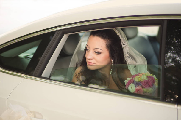 aantrekkelijke Kaukasische bruid zitten in auto en glimlach naar de camer - Foto, afbeelding