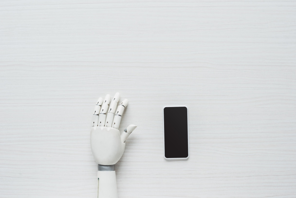 cropped image of prosthetic arm and smartphone with blank screen at wooden table  - Foto, immagini