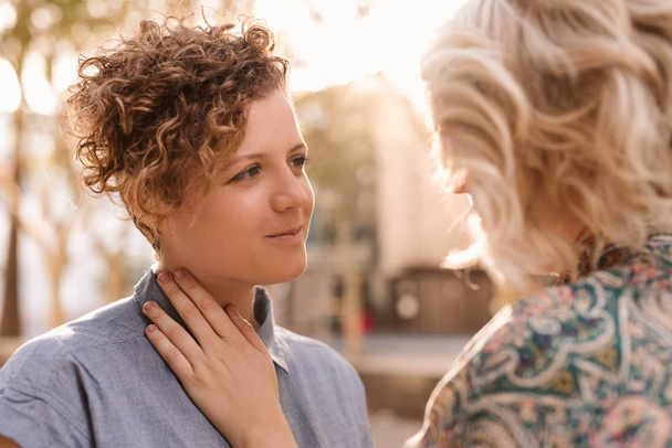 Romantic young lesbian couple staring into each other's eyes while standing face in face together on a sunny city street - Photo, image