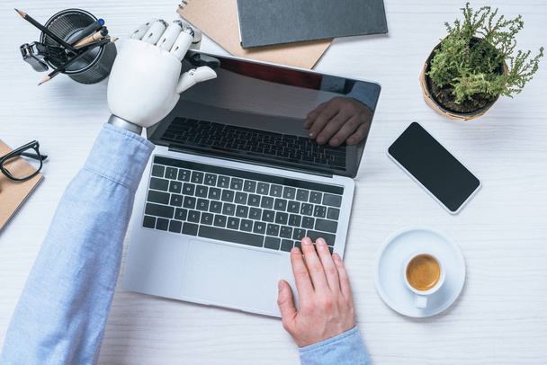 частичный взгляд бизнесмена с протезом руки, открывающего ноутбук за столом в офисе
  - Фото, изображение