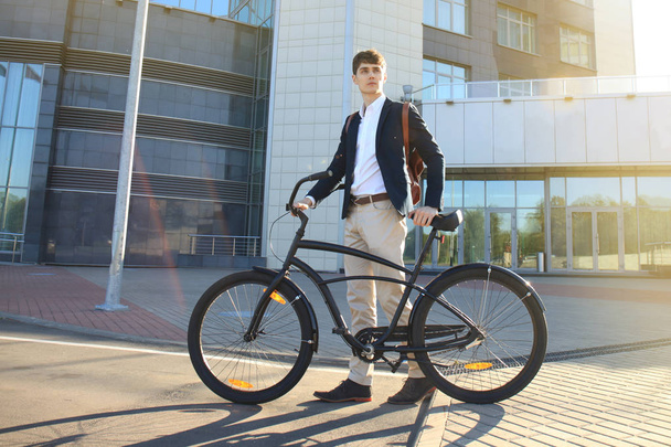 Confident young businessman walking with bicycle on the street in town - Foto, Imagen