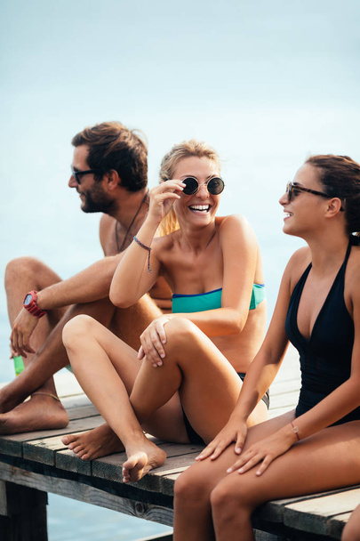 Group of smiling people in swimwear sitting on deck and enjoying summertime together. - 写真・画像
