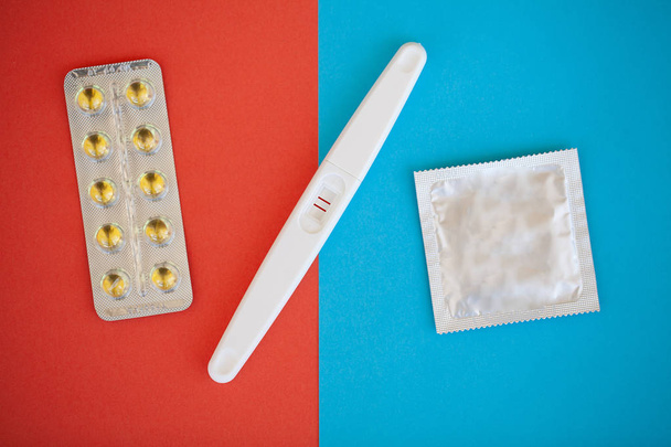 Zwangerschapstest. Het resultaat is positief met twee strips en condoom met anticonceptiva op gekleurde achtergrond pil van de Geboortenbeperking, veilige seks, gezondheidszorg concep - Foto, afbeelding