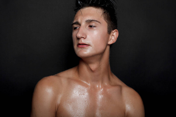 people, skincare and beauty concept - Wet young man with black hair on a black background. Portrait male with shaved chest . Men's skin care. Ripped muscular handsome man on black background - Zdjęcie, obraz