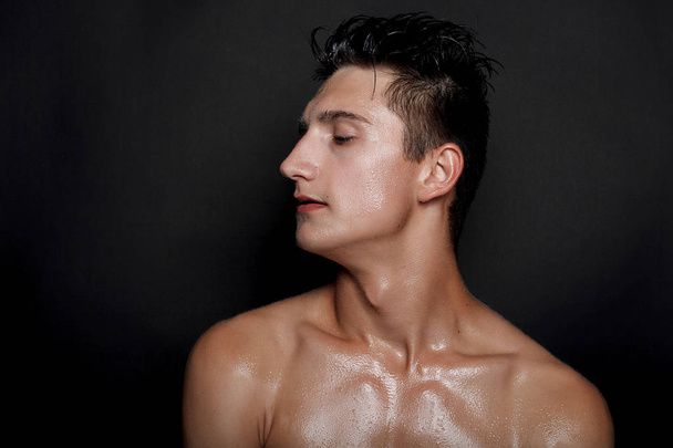 people, skincare and beauty concept - Wet young man with black hair on a black background. Portrait male with shaved chest . Men's skin care. Ripped muscular handsome man on black background - 写真・画像