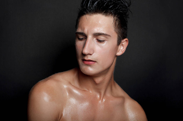 people, skincare and beauty concept - Wet young man with black hair on a black background. Portrait male with shaved chest . Men's skin care. Ripped muscular handsome man on black background - Photo, Image