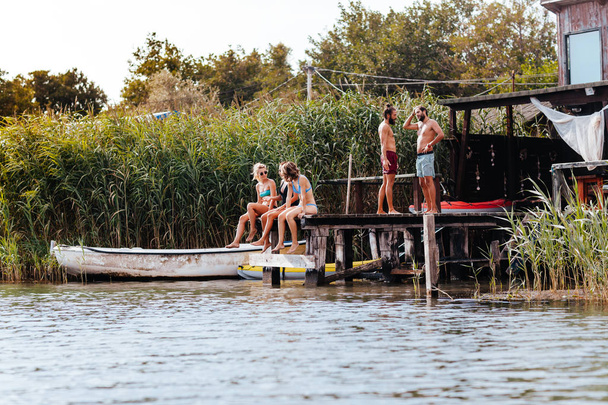 Grupo de jovens em roupa de banho desfrutando de férias de verão na margem do rio
. - Foto, Imagem