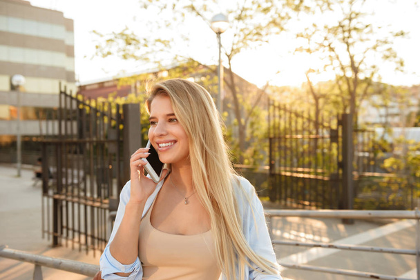 Image of cheerful woman outdoors talking by mobile phone looking aside. - Photo, image
