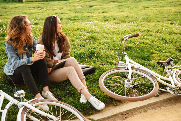 Photo of two young happy women friends outdoors with bicycles in park. - Fotografie, Obrázek