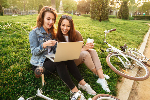 Obrázek dvou přátel mladé krásné šťastné ženy venku pomocí přenosného počítače v parku. - Fotografie, Obrázek