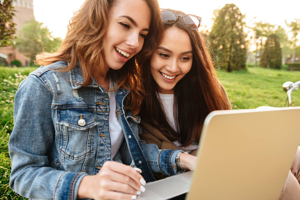 Image of two young beautiful happy women friends outdoors using laptop computer in park. - Fotografie, Obrázek