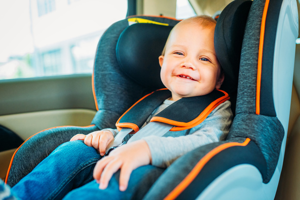 bebê pequeno feliz sentado no assento de segurança da criança no carro e olhando para a câmera
 - Foto, Imagem