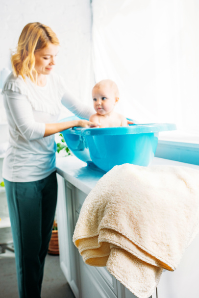young mother bathing child in plastic bathtub at home - Foto, imagen