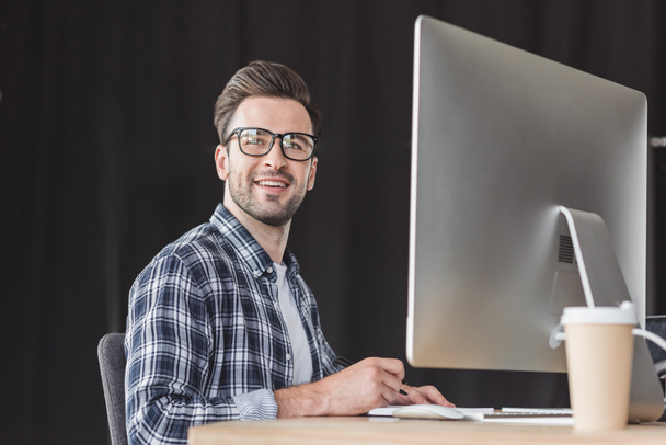guapo sonriente joven programador en gafas de trabajo con ordenador de sobremesa
 - Foto, imagen