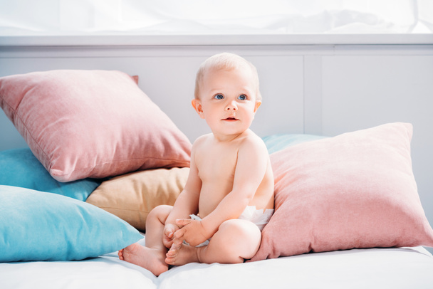щаслива маленька дитина сидить у ліжку з великою кількістю подушок і дивиться вгору
 - Фото, зображення