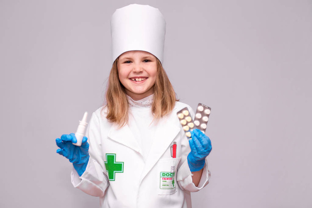 Usměvavá holčička v lékařských uniformě Držte nosní sprej a pilulky pro zdraví. Dívka doktor doporučuje lék sprej - Fotografie, Obrázek