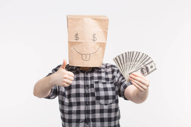 白い背景の上に親指を現して紙幣との幸せなペーパー バッグ マスクの男性 - 写真・画像