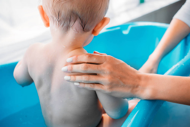 tiro cortado da mãe lavar seu filho na banheira de plástico do bebê em casa
 - Foto, Imagem