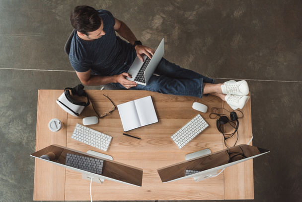 Overhead-Ansicht eines jungen Mannes mit Laptop und Desktop-Computern am Arbeitsplatz  - Foto, Bild