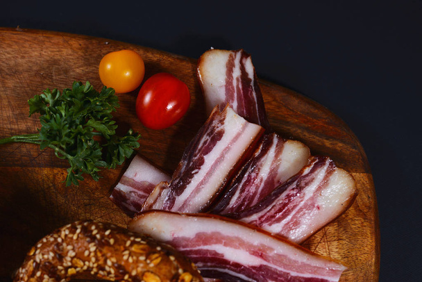 Wooden board with slice of bacon, parsley and tomatoes. - Foto, imagen