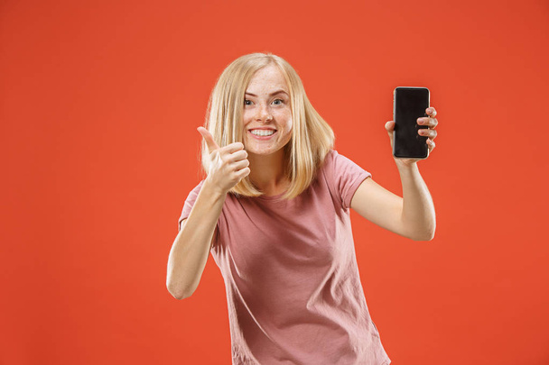 Portrait of a confident casual girl showing blank screen mobile phone isolated over red background - Zdjęcie, obraz