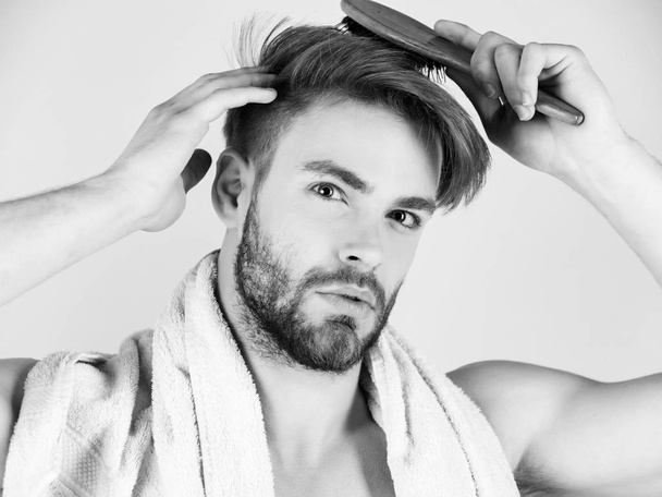 człowiek troszczy się o jego włosy. Brodaty mężczyzna z kąpielowy ręcznik na szyi, czesanie włosów zdrowych - Zdjęcie, obraz