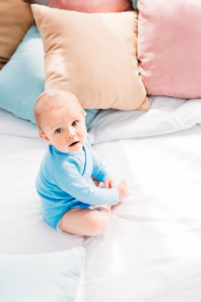 high angle view of adorable little baby sitting in bed and looking at camera - Fotografie, Obrázek