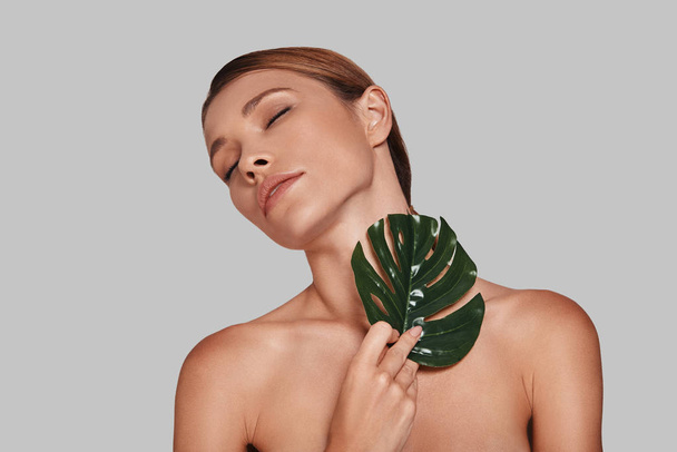 caucasian model young woman keeping eyes closed and covering neck with leaf in studio  - Photo, Image