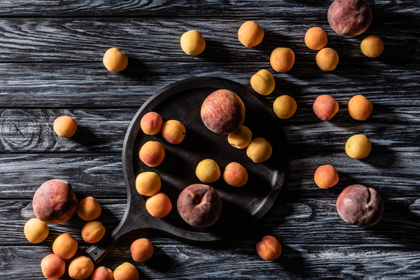 Blick von oben auf Haufen von Aprikosen und Pfirsichen in der Nähe Tablett auf Holztisch  - Foto, Bild