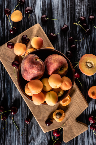 elevated view of bowl with apricots and peaches surrounded by cherries on wooden talbe  - Foto, imagen
