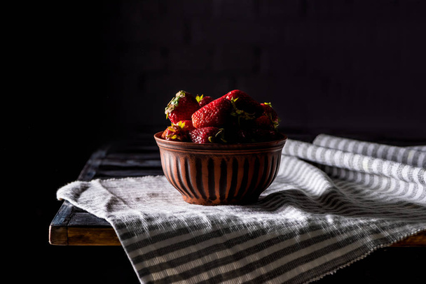 close up view of bowl with pile of strawberries on wooden table on black - Fotó, kép