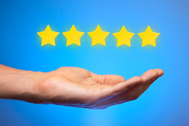 Five golden yellow stars out of five. Man holds star on the palm of his hand, puts rating, reviews - Photo, Image