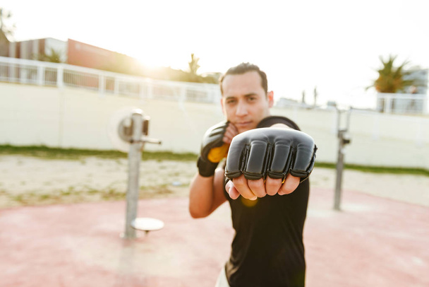 Photo of young concentrated strong sports man boxer outdoors make exercises in gloves. - Photo, Image