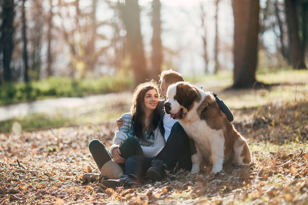 Young couple enjoying nature outdoors together with their adorable Saint Bernard puppy. People and dogs theme. - Foto, imagen