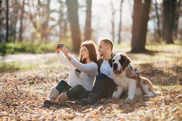 Young couple enjoying nature outdoors together with their adorable Saint Bernard puppy. People and dogs theme. - Foto, Bild