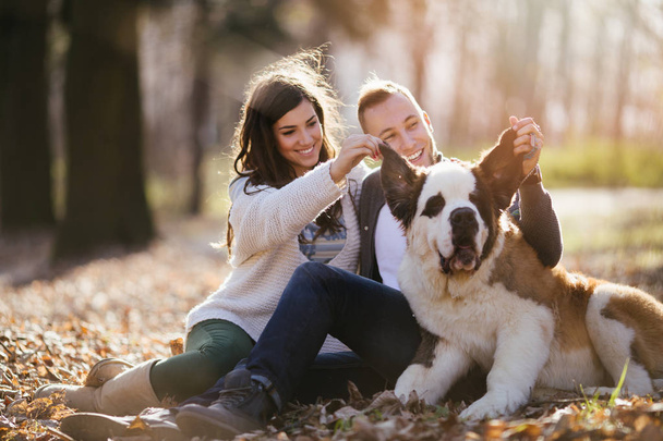 Young couple enjoying nature outdoors together with their adorable Saint Bernard puppy. People and dogs theme. - Φωτογραφία, εικόνα