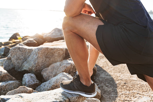 Cropped image of a sportsman doing stretching exercises at the seaside in the morning - Foto, afbeelding