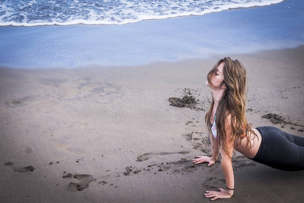 Młoda kobieta piękny model kaukaski czy Pilates na brzegu na plaży. piasek i suche lato mokry wypoczynku. ładne ciało z zewnątrz życia fitness i ćwiczenia - Zdjęcie, obraz