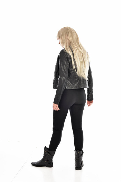 full length portrait of blonde girl wearing black leather clothes. standing pose with back to the camera. isolated on white studio background. - Fotografie, Obrázek
