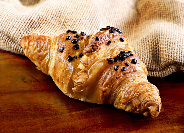 Delicious chocolate croissant with chocolate topping. Gourmet eating scene with wooden table and fresh butter croissant. - Photo, Image