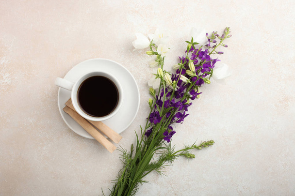 ein schöner Strauß Glockenblumen und eine Tasse Tee auf neutralem Hintergrund. Ansicht von oben, Kopierraum.  - Foto, Bild