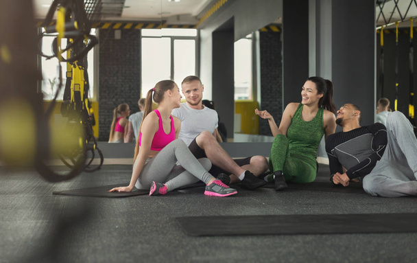 Group of young sporty smiling people sitting on floor, talking after workout, friends having rest before fitness class, copy space - Foto, imagen