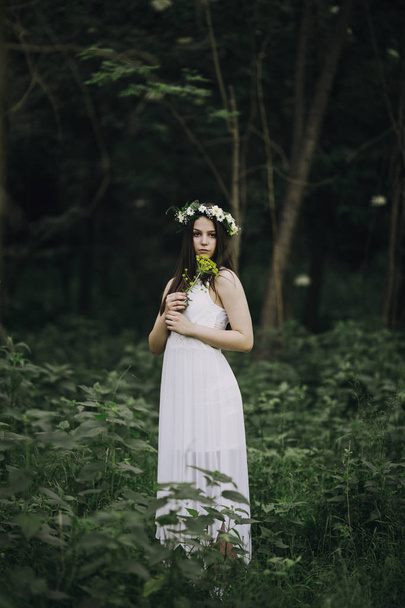 Fine art outdoor portrait of beautiful young woman in a white dress wearing floral wreath - Fotó, kép