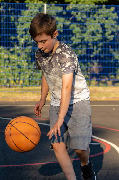 Pre-teen boy playing with a basketball in a park - Фото, изображение