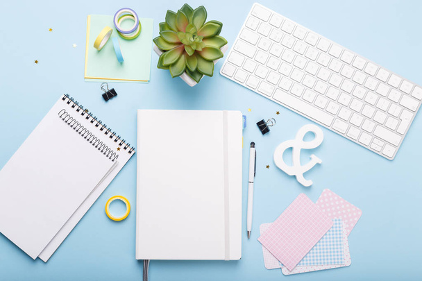 Espaço de trabalho com teclado, diário, caneta, clipes de papel, adesivos em tendência fundo azul, flat lay
 - Foto, Imagem