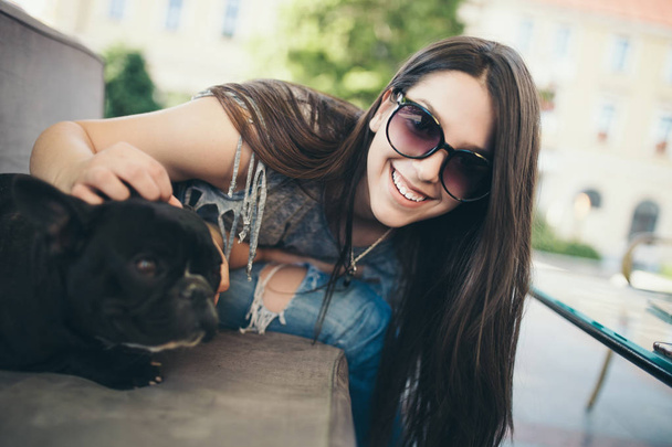 Cute teenager girl enjoying outdoors in cafe bar together with her adorable French bulldog puppy. Strong back light. Warm sunny day. - Foto, Imagem
