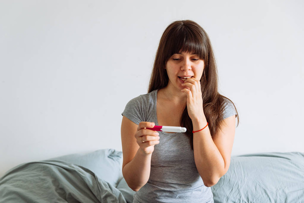 kadın yatakta otururken hamilelik testi seyir endişeli manzaralı - Fotoğraf, Görsel
