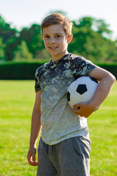 Vorpubertärer Junge hält einen Fußball in einem Park - Foto, Bild