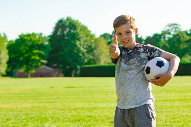 Pre-teen boy holding a football in a park - Foto, afbeelding