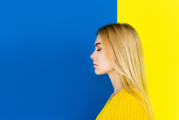 Portrait of girl with closed eyes wearing yellow clothes isolated on blue and yellow background - Φωτογραφία, εικόνα